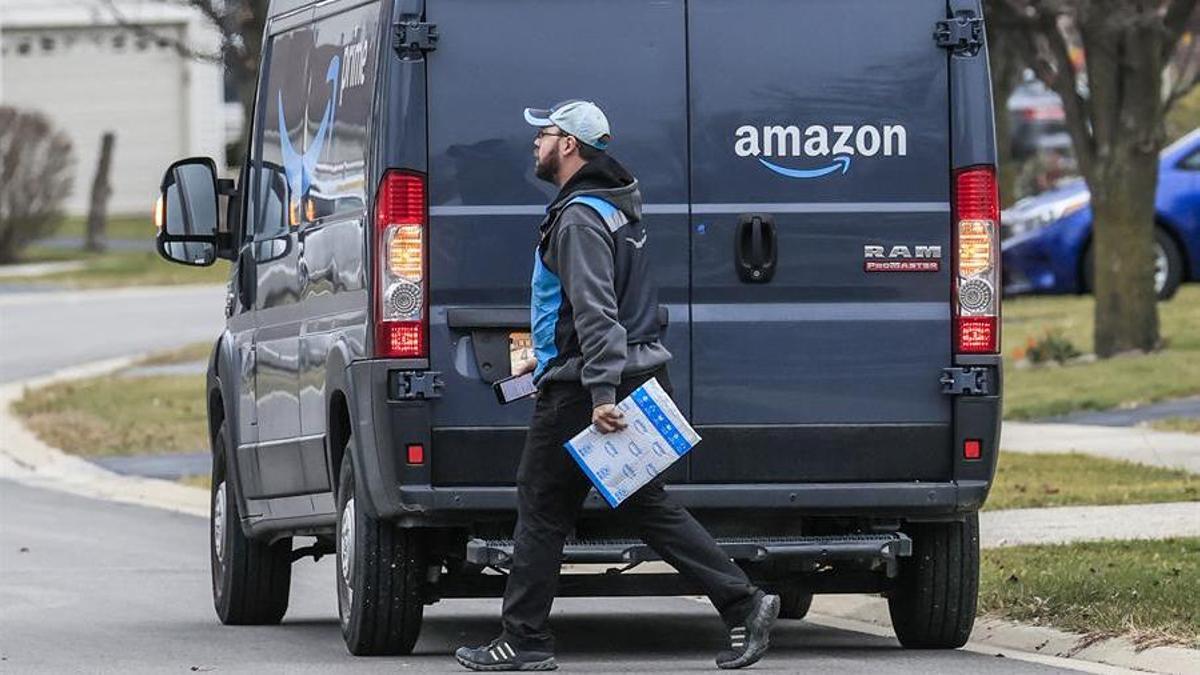 Un repartidor pasa frente a una furgoneta con el logo de Amazon.
