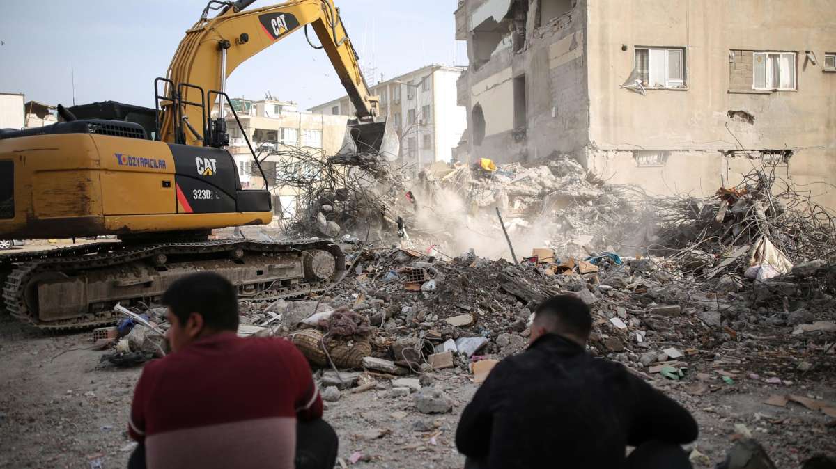 Dos hombres observan los trabajos de retirada de escombros en una de las zonas devastadas por el terremoto en Turquía.