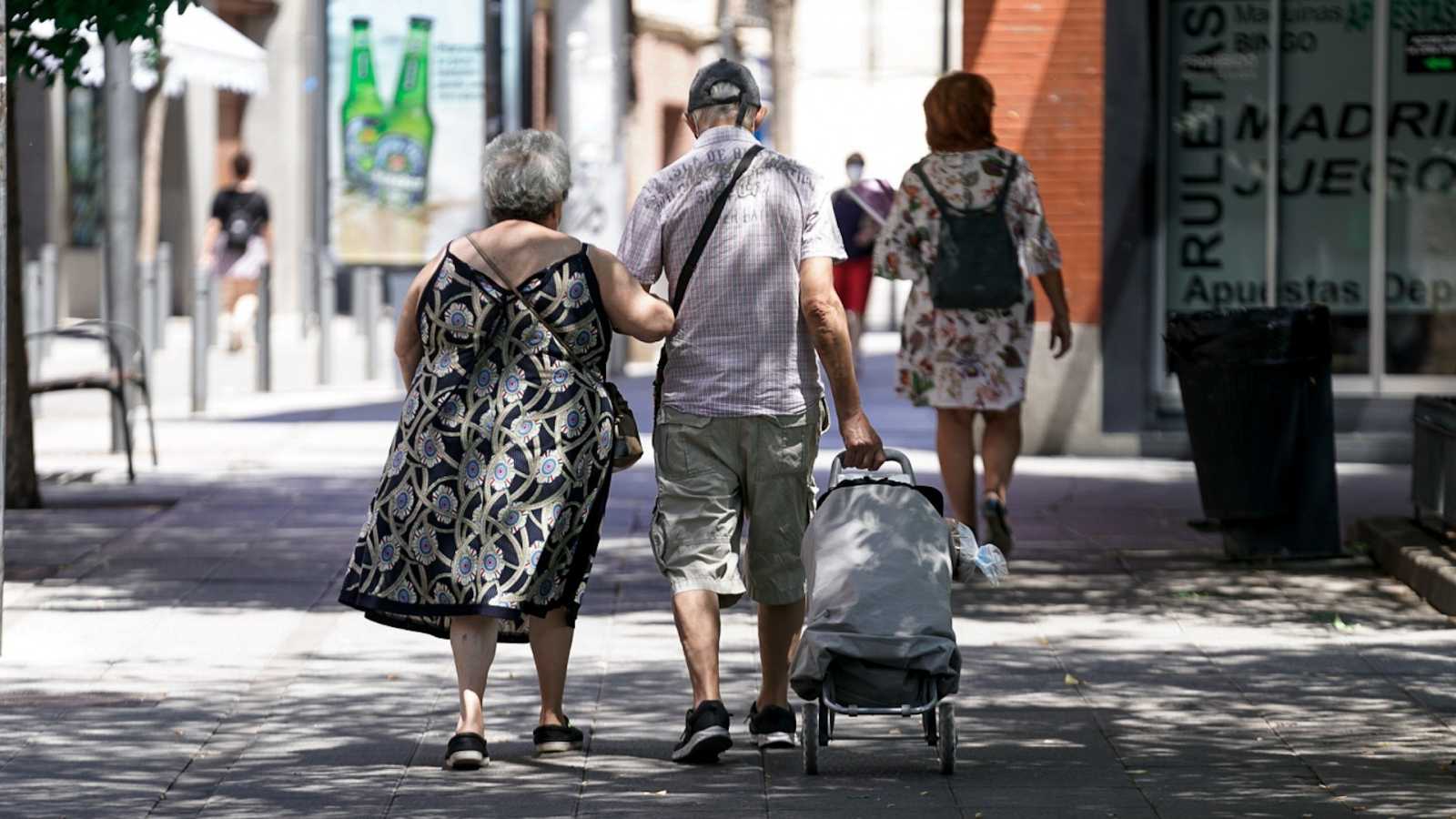 Una pareja de ancianos camina por las calles de Madrid con el carro de la compra.