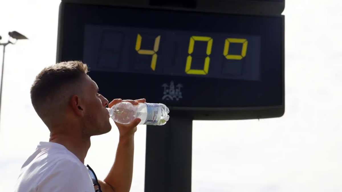 Un joven bebe agua junto a un termómetro de calle que marca 40 grados en el centro de Córdoba.