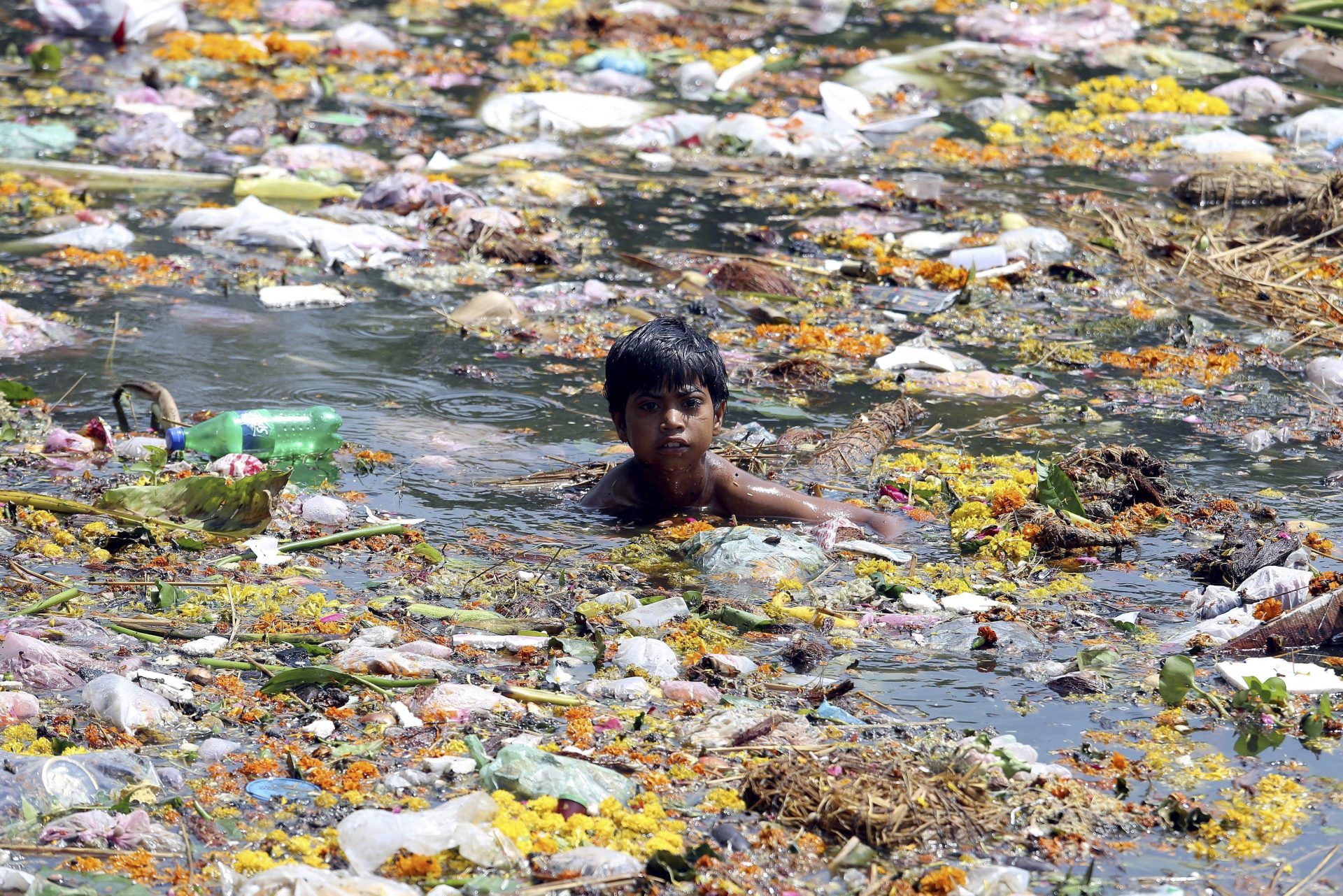Un joven trapero nada entre residuos plásticos que flotan en un lago en Bhopal, India.