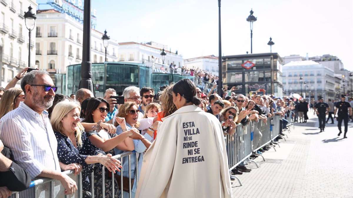 Villacís, con su 'abrigo pancarta', saluda a los vecinos presentes en la Puerta del Sol en la Fiesta del 2 de Mayo.