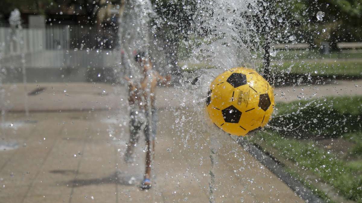 Unos niños juegan a la pelota mientras se refrescan en una fuente del barrio del Zaidín, en Granada.