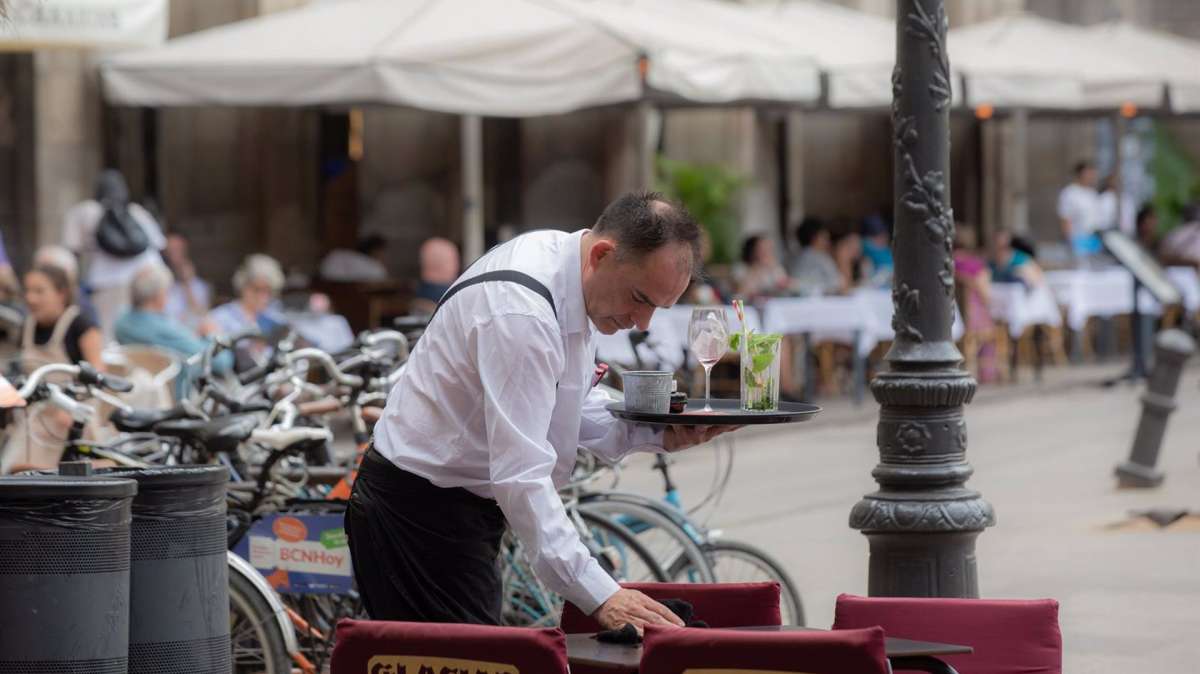 Un camarero limpia una mesa en la plaza Real de Barcelona.