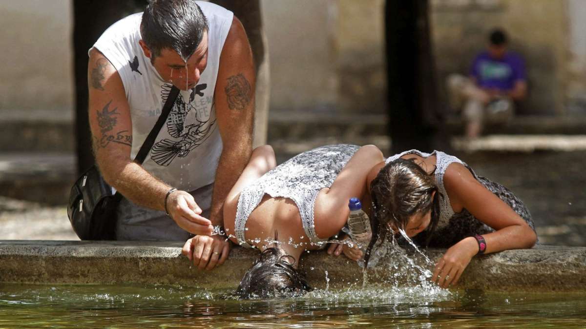 Tres personas se refrescan en una fuente durante una de las sucesivas olas de calor del verano.